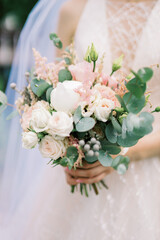 Wedding bouquet of peony rose, rose and eucalyptus in the hands of the bride. European style wedding. Selected focus and blurred background.