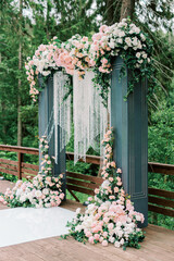 Fototapeta na wymiar Modern ceremony in European style. Wedding arch with roses on the background of a forest lake and trees. Jewelry from natural flowers and crystals. Side view
