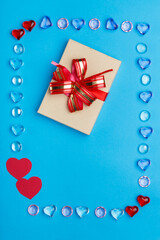 In a frame made of pebbles of hearts on a blue background, a box with a bow. Copy the place.
