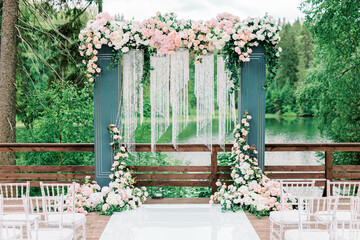 Modern ceremony in European style. Wedding arch with roses on the background of a forest lake and...