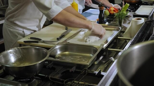 Close-up of the chef sprinkling salt on raw fish before baking in the oven. The process of cooking Dorado fish in a large amount of salt in a professional kitchen.