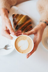 Girl in a cafe with a hot cup of latte coffee and croissant