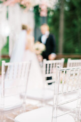 Modern ceremony in European style. Transparent plastic chairs with a padded base for guests stand against the wedding arch. Selected focus and blurred background.