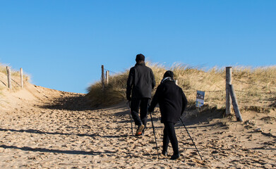 Vendée, France; January 25, 2021: A couple of Nordic walkers enjoying the good weather come back from the beach, Bretignolles Sur Mer.
