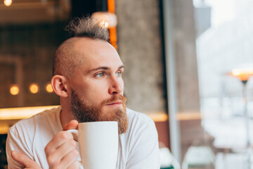 Brutal man of European appearance in a cafe in the morning with a cup of hot coffee