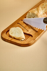 A cut baguette and a piece of bread lies next to a white ceramic knife on a bamboo cutting board