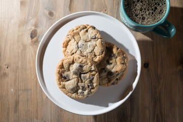 Chocolate chips cookies on a plate with coffee in a mug.