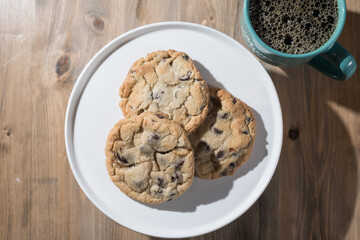 Chocolate chips cookies on a plate with coffee in a mug.