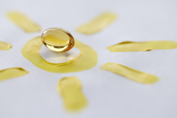 Yellow transparent vitamin D pill lying on drawn sun closeup