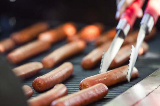 Selective focus shot of man hands grilling sausages on the barbecue grill