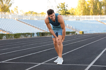 Man in sportswear having knee problems at stadium