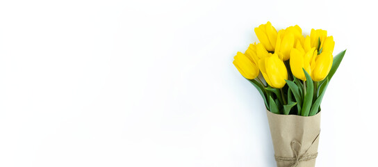 Bouquet of yellow tulips wrapped in craft paper on white background with copy space.