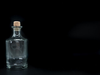 Single empty glass bottle on a black background. Transparent square bottle. Front view of the laying on its side transparent square bottle.