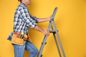 Professional builder climbing up metal ladder on yellow background, closeup