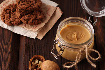 Glass jar with natural nut butter, healthy cookies, walnuts on a brown wooden background. Vegetarian traditional breakfast close up.