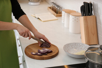 Woman cutting red onion into slices at table in kitchen, closeup