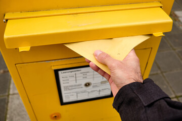 Nuremberg, Germany - December 03, 2019: hand putting an envelope into the mail slot of a yellow...