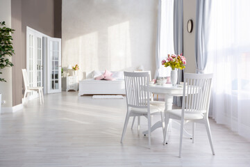 Luxurious and expensive interior of an open-plan apartment in light colors. Stylish modern bedroom with minimal design, dining area and guest space.