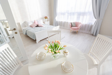 Luxurious and expensive interior of an open-plan apartment in light colors. Stylish modern bedroom with minimal design, dining area and guest space.