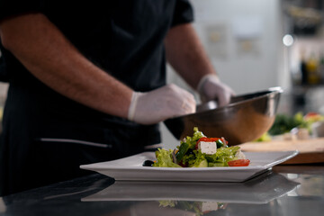 chef cook hands in gloves prepare or put healthy greek salad on plate at kitchen