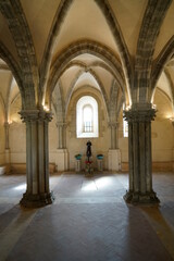 sala capitolare di un ' abbazia medievale con colonne , archi che si incrociano sul soffitto , bella l ' illuminazione e finestra in controluce