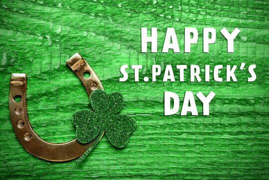 Happy St. Patrick's Day. Golden horseshoe and decorative clover leaf on green wooden table, flat lay