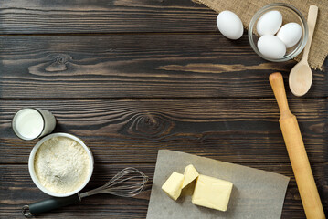 Eggs, flour, butter, whisk and milk on a wooden table.