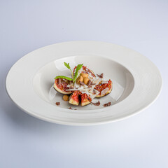 White plate with a fig or breva divided into four pieces decorated with coconut and mint, delicious combination of color and texture in a sweet dessert