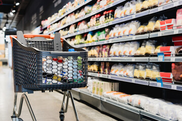 Shopping cart near packages on shelves in supermarket - Powered by Adobe