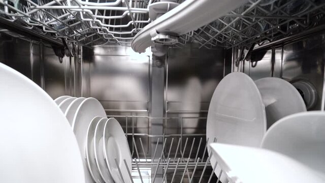 Backward dolly shot of dishwasher machine from inside, with dishes and silverware