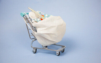 Shopping cart and medicine. An expensive medicine. Cough pills shopping basket with thermometer and medicine mask on blue background.