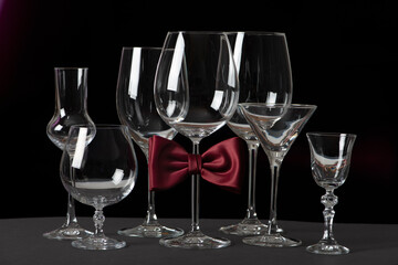 Alcohol glasses with bow tie isolated on black background. International Bartenders Day.