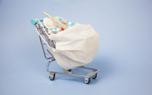 Shopping Cart And Medicine. An Expensive Medicine. Cough Pills Shopping Basket With Thermometer And Medicine Mask On Blue Background.