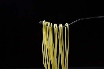 Spaghetti on a black background. Boiled spaghetti on a fork. Isolated spaghetti. Spaghetti hanging on a fork