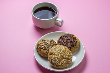 Shortbread cookies on a pink background. Shortbread cookies with sprinkles on a white plate. Cup of coffee with dessert