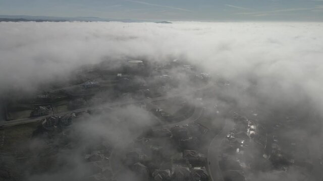 Wide angle drone footage through the cloud line on a bright sunny morning over Folsom, USA with scattered fog and mountains in the background