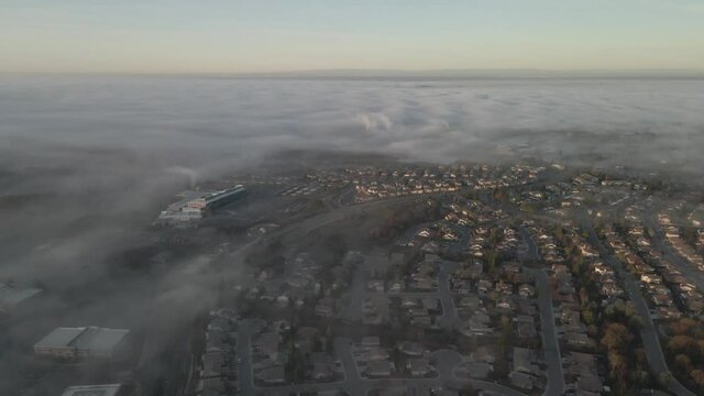 Dreamy drone wideangle footage over Folsom, USA showing houses and streets through the low lying misty clouds, and pastel coloured mountains in the distance
