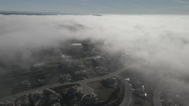 Drone footage through cloud line on a misty morning, showing Folsom, USA in breaks through the clouds revealing a neighborhood below.