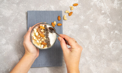Girl picks a spoonful of chia pudding dessert, yogurt, fruits, seeds and nuts on a concrete background with copy space