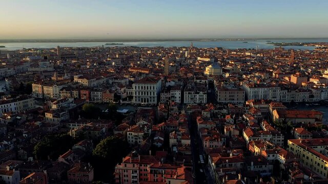 Beautiful panoramic aerial drone footage of Venice architecture during sunset. Drone going down over canals and roofs.