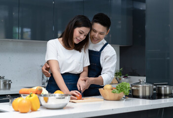 Portrait of Asian couple in love standing close together, cuddling and caringly, cooking at kitchen table. Couple spending time together at home.