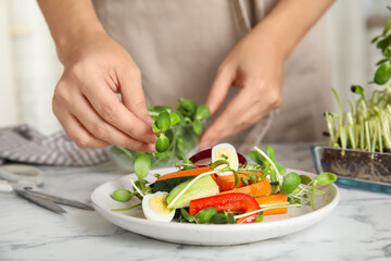 Woman making salad with fresh organic microgreen at white marble table, closeup