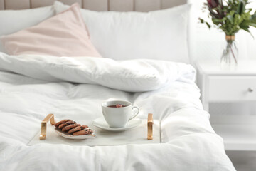Cup of aromatic tea and cookies on soft blanket in bedroom