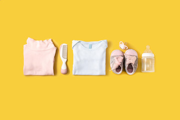 Baby rompers, shoes, feeding bottle, pacifier and hair comb on yellow background