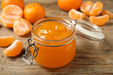 Tasty tangerine jam in glass jar on wooden table