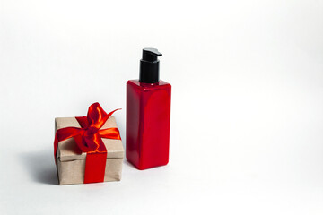 A red bottle of lotion next to a gift box tied with a red ribbon on a white background. copy space