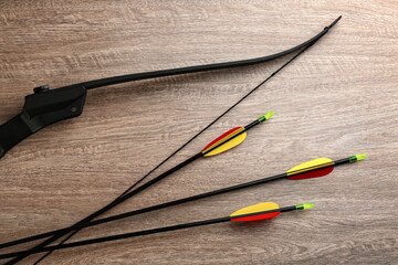 Plastic arrows and bow on wooden table, flat lay. Archery sports equipment