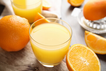 Fresh ripe oranges and glass of juice on wooden table, closeup