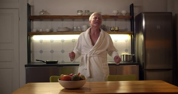 Funny Senior Man Wearing Bathrobe Dancing In Modern Kitchen Alone