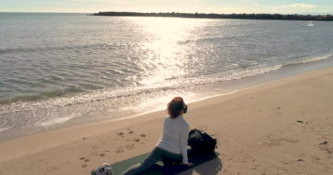 mujer senior haciendo posturas de yoga y meditaci&oacute;n en estera en la arena de la playa